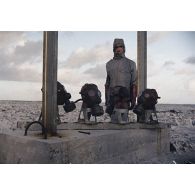 Près du poste d’enregistrement avancé (PEA) Denise, des personnels en tenue NBC relèvent des masques à gaz exposés pour étude des effets des tirs par la section technique de l’armée de terre (STAT).