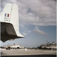 Au premier plan, la queue d'un avion DC-6. Les bâtiments-bases (BB) Maurienne (A637) et Moselle (A608), et le bâtiment de soutien logistique (BSS) Rance (A618) à quai au port, probablement sur la base avancée du Centre d'expérimentations du Pacifique (CEP) sur l'atoll d'Hao ou à Moruroa.