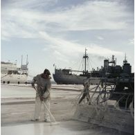 Activité de peinture sur un quai du port. En arrière-plan, le bâtiment-base (BB) Maine (A611) et le bâtiment de soutien logistique (BSS) Tarn (A771) à quai, probablement sur la base avancée du Centre d'expérimentations du Pacifique (CEP) sur l'atoll d'Hao ou à Moruroa.