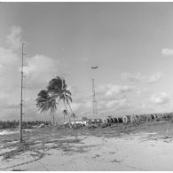 Préparatifs et mise en place des matériels pour le tir d'essai nucléaire Licorne du 3 juillet 1970 à Moruroa (Mururoa). Vue du ballon captif en vol, dans le secteur de la zone Dindon, au-dessus d'un blockhaus de poste d'enregistrement avancé (PEA) et d'une tour  à antennes.