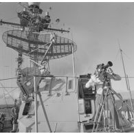 A bord du croiseur de commandement De Grasse : un caméraman est posté derrière sa caméra sur trépied devant les groupes radar et antenne en aérien lors du tir Licorne du 3 juillet 1970.