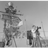 A bord du croiseur de commandement De Grasse : un caméraman est posté derrière sa caméra sur trépied devant les groupes radar et antenne en aérien lors du tir Licorne du 3 juillet 1970.