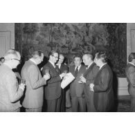 Robert Galley, ministre des Armées, donne un cocktail en l'honneur des journalistes spécialisés ayant participé au voyage en Polynésie française, et reçoit leurs voeux dans les salons de l'hôtel de Brienne. Consultation d'un journal.