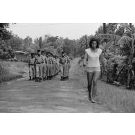 Défilé des troupes à l'issue de la cérémonie de remise de la fourragère à de jeunes marsouins du régiment d’infanterie de marine du Pacifique - Polynésie (RIMAP-P) à Taravao. Une femme marche sur la route.