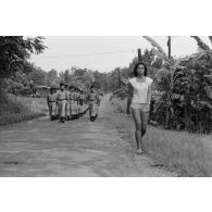Défilé des troupes à l'issue de la cérémonie de remise de la fourragère à de jeunes marsouins du régiment d’infanterie de marine du Pacifique - Polynésie (RIMAP-P) à Taravao. Une femme marche sur la route.