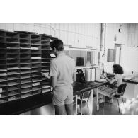 Le groupement de transmission terre (GTT) 815 à l'état-major du Taaone : commandement, exploitation, centre de relais bande. Un caporal féminin place une capsule dans le réseau de transport par tube pneumatique (air comprimé).