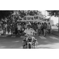 A Papeete, un motard de la police municipale encadre une manifestation antinucléaire dont les participants portent une banderole énonçant  "ia ora te natura" (vive la nature).