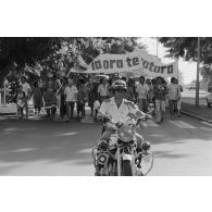 A Papeete, un motard de la police municipale encadre une manifestation antinucléaire dont les participants portent une banderole énonçant  "ia ora te natura" (vive la nature).