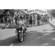 A Papeete, un motard de la police municipale encadre une manifestation antinucléaire dont les participants portent une banderole énonçant  "ia ora te natura" (vive la nature).