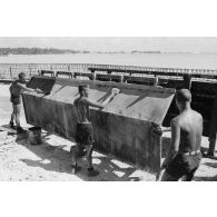 A Moruroa, édification d'un mur de protection contre les raz de marée par le 5e régiment mixte du Pacifique (5e RMP). Un légionnaire applique un enduit sur la paroi métallique d'un élément de coffrage, ses collègues décapent les résidus de béton.