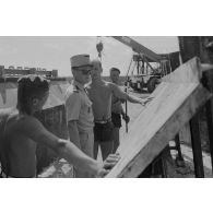 A Moruroa, édification d'un mur de protection contre les raz de marée par les légionnaires du 5e régiment mixte du Pacifique (5e RMP). Un officier inspecte les résidus de béton sur la paroi métallique d 'un élément de coffrage.