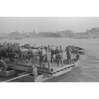 Des soldats et des chevaux traversent le cours d’eau à bord d’une barge.