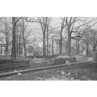 Tas de débris et de bois, jardin et bâtiment en ruine.