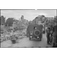 Le général de division Alphonse Augustin, commandant la 3e division d'infanterie algérienne (3e DIA), circule dans un convoi à bord de sa jeep au milieu des ruines d'une commune.