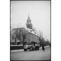 Un half-track dans une rue d'une commune ; à l'arrière-plan, une église protestante.
