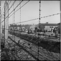 Dans le camp de concentration de Dachau libéré, des déportés rescapés attendent derrière les barbelés, près des baraquements.