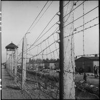 Dans le camp de concentration de Dachau libéré, des déportés rescapés attendent derrière les barbelés, près des baraquements.