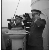 Un capitaine de vaisseau et un lieutenant de vaisseau observent l'horizon aux jumelles sur la passerelle du torpilleur Bouclier ou Flore.