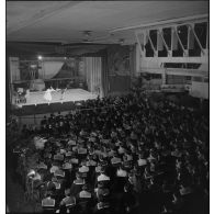 Vue en plongée sur l'équipage du porte-avions Béarn rassemblés dans une salle à l'occasion d'une représentation théâtrale donnée sur le navire le soir, la veille de Noël.