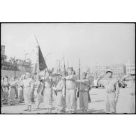 Le drapeau du 1er régiment de tirailleurs algériens (1er RTA) et sa garde au présentez-armes sur un quai du port d'Alger.
