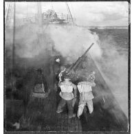 Des canonniers ouvrent le feu sur un objectif avec un canon antiaérien de 37 mm à bord d'un cargo naviguant en convoi, réquisitionné et armé par la Marine nationale.