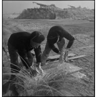 Des marins canonniers d'une batterie de défense côtière lavent leur linge. A l'arrière-plan, des canons de 155 mm.