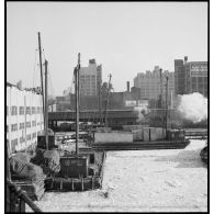 Dans le port de New-York pris par les glaces, des chalands transportent des caisses contenant des avions destinés aux Alliés, qui vont être chargées sur des cargos.