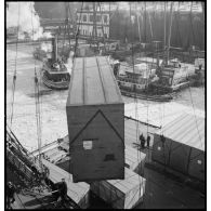 Dans le port de New-York pris par les glaces, des caisses qui contiennent des avions destinés aux Alliés sont chargées à bord d'un cargo.