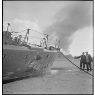 Avant tribord du chasseur de sous-marins CH 9 échoué sur la plage de Malo-les-Bains. A l'arrière-plan, la ville de Dunkerque en flammes.