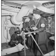 L'aumônier du cuirassé Dunkerque en tenue d'alerte s'entretient avec un médecin et infirmier du bord.