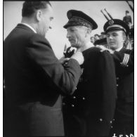 Louis Jacquinot, ministre de la Marine, remet l'insigne de commandeur de la Légion d'honneur au contre-amiral Robert Jaujard lors d'une cérémonie à bord d'un bâtiment.