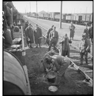 Des soldats perçoivent leur ration pour le repas le long d'une voie ferrée en gare de Trappes.