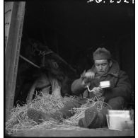 Un soldat mange assis à la porte d'un wagon de marchandises.