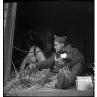Un soldat mange assis à la porte d'un wagon de marchandises.