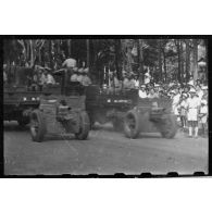Passage de pièces d'artillerie tractées par des camions de transport lors du défilé du 14 juillet 1946 à Saigon.