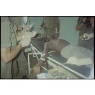 Intervention et opération chirurgicale sur un patient blessé à la main dans un dispensaire à Karama par les membres de l'antenne chirurgicale parachutiste (ACP).