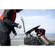 Des techniciens audiovisuels installent une antenne satellite sur le pont d'envol du porte-hélicoptèress amphibie (PHA) Tonnerre à Sète.
