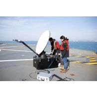 Des techniciens audiovisuels installent une antenne satellite sur le pont d'envol du porte-hélicoptèress amphibie (PHA) Tonnerre à Sète.