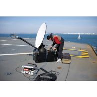 Un technicien audiovisuel installe une antenne satellite sur le pont d'envol du porte-hélicoptèress amphibie (PHA) Tonnerre à Sète.
