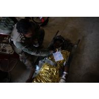 Une auxiliaire sanitaire du Service de santé des armées (SSA) encadre un soldat simulant une blessure grave pour son évacuation depuis le Rôle 1 de Saint-Germainmont.