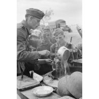 Des fantassins de la 137. infanterie division patientent devant une cuisine roulante.