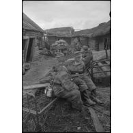 Alors que les Nashorn avancent prudemment, des fantassins patientent entre deux isbas abandonnées.