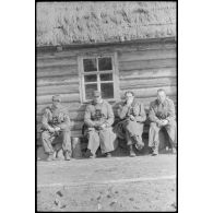 Un sous-officier et trois officiers marquent une pause devant une isba.