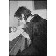 Portrait d'une femme répondant à des questions et rédigeant un courrier, il pourrait s'agir d'un interrogatoire.