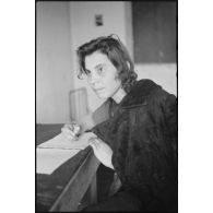 Portrait d'une femme répondant à des questions et rédigeant un courrier, il pourrait s'agir d'un interrogatoire.