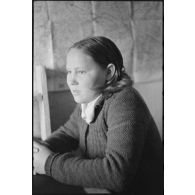 Portrait d'une jeune femme répondant à des questions, une carte est accrochée sur le mur.