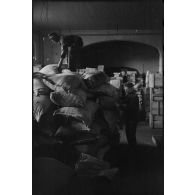 Au sein d'un magasin d'approvisionnement, des soldats entassent des sacs de farine.