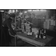 Un officier récupère sa commande, les vivres sont rassemblés sur une table et contrôlées par le personnel du magasin.