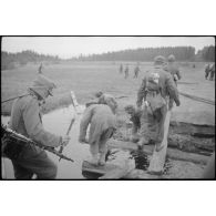 Alors que villageois requis réparent un pont de bois, des fantassins allemands le traversent.