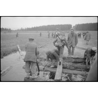 Alors que villageois requis réparent un pont de bois, des fantassins allemands le traversent.